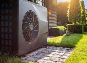 The outside box unit of a mini split heat pump system sitting amongst lush green grass.